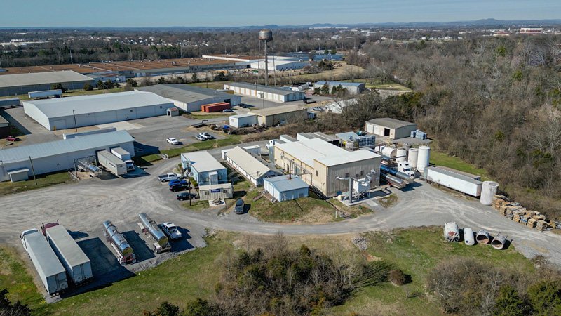 An aerial view of an industrial facility featuring large storage tanks, a truck, and connected piping on a sunny day